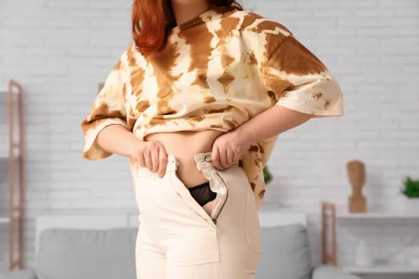 Image of woman trying to do her trousers up after pregnancy weight gain Richmond upon Thames