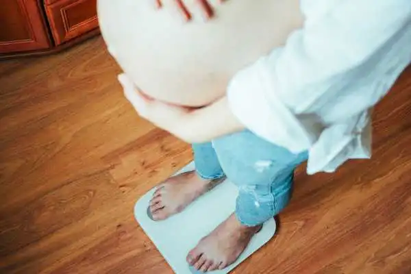Image of woman weighing herself and experiencing weight gain through pregnancy Richmond upon Thames